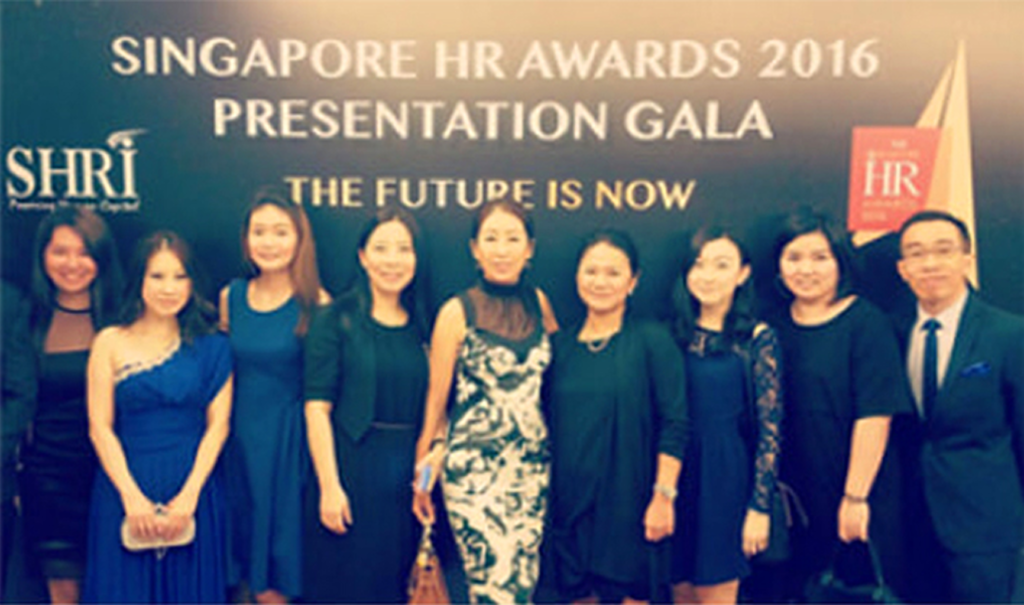 A group of nine people in formal attire pose together at the Singapore HR Awards 2016 Presentation Gala, standing in front of an event backdrop.