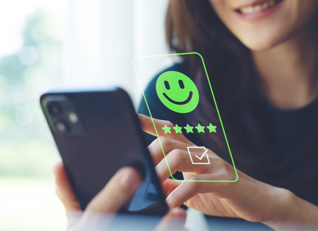 A woman holds a smartphone and interacts with a virtual screen displaying a green smiley face, five stars, and a checkmark, indicating a positive online review or rating.
