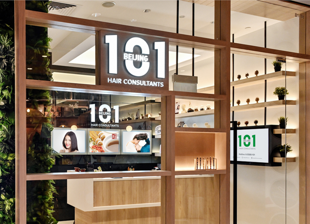A modern storefront for Beijing 101 Hair Consultants with a well-lit sign, glass windows, and a clean interior featuring product displays and images of people on the back wall.