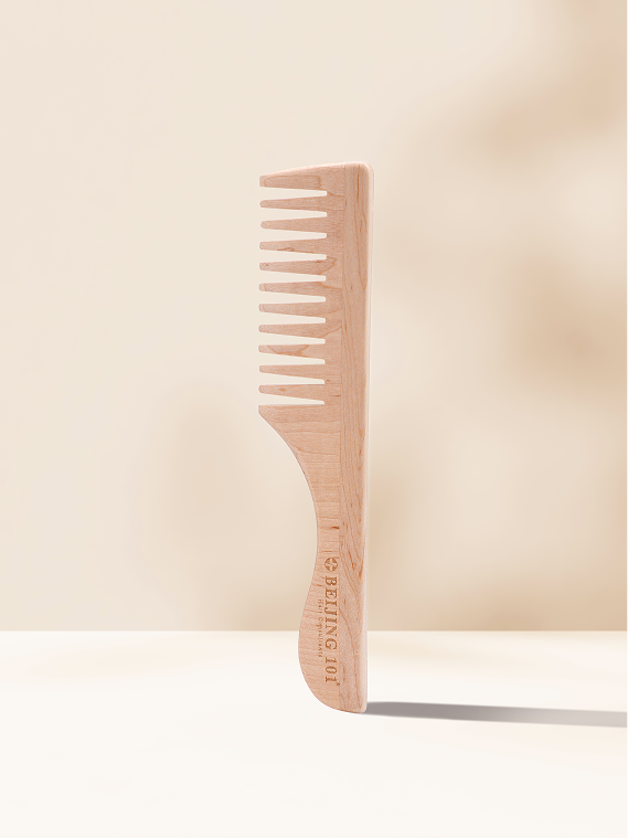 The Beijing 101 Wide Tooth Wooden Comb stands upright on a light surface against a neutral beige background, featuring “BEIJING 101” engraved on its handle for a subtle touch of elegance.