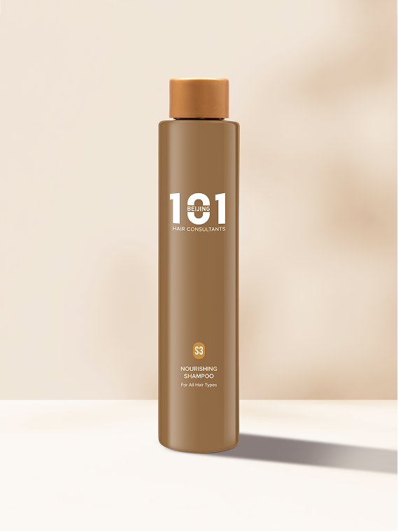 A tall brown bottle of Beijing 101 Nourishing Shampoo 250ml with a gold cap stands upright on a light-colored surface against a beige background.