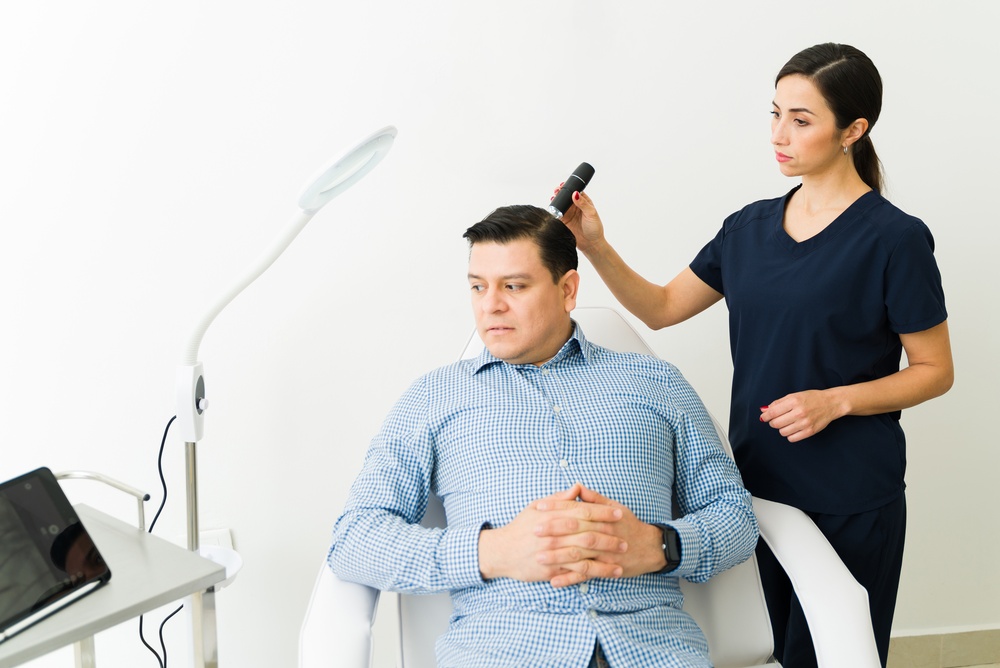 A healthcare professional examines a seated man’s scalp with a handheld device in a modern, well-lit clinic, checking for early signs of hair loss to determine if it may be temporary or permanent.